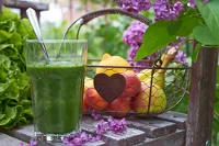 Ein Glas mit Grünem Smoothie vor Obstkorb