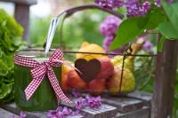 Ein Glas mit Grünem Smoothie und Schleifchen vor Obstkorb